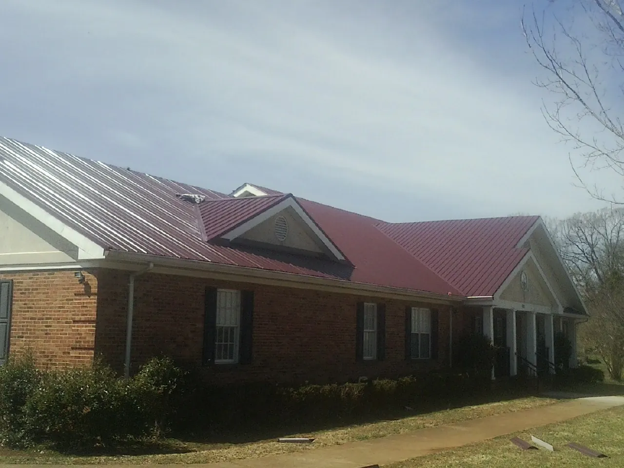 Red metal roof with gabled entries on a long brick building, from a Hail Damage Roof Repair job in Sedro Woolley