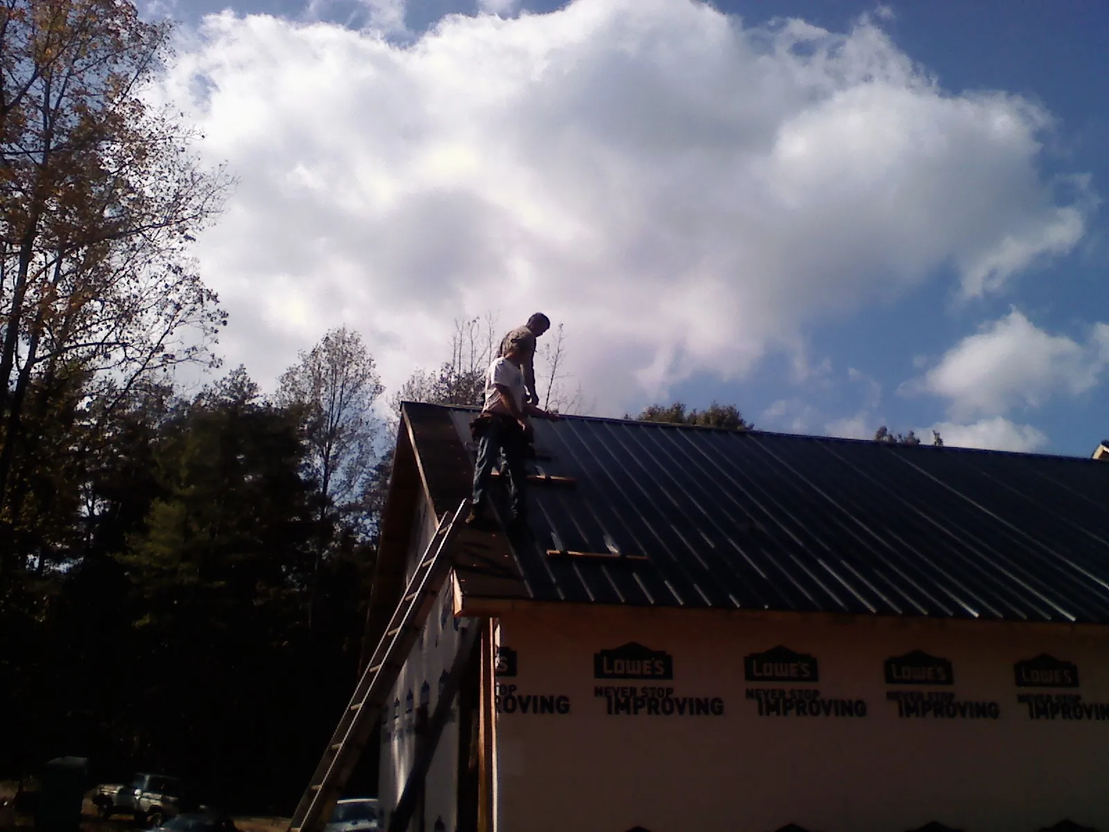 Roofer fastening dark metal panels high against a cloudy sky, from a Roof Inspection job in Sedro Woolley