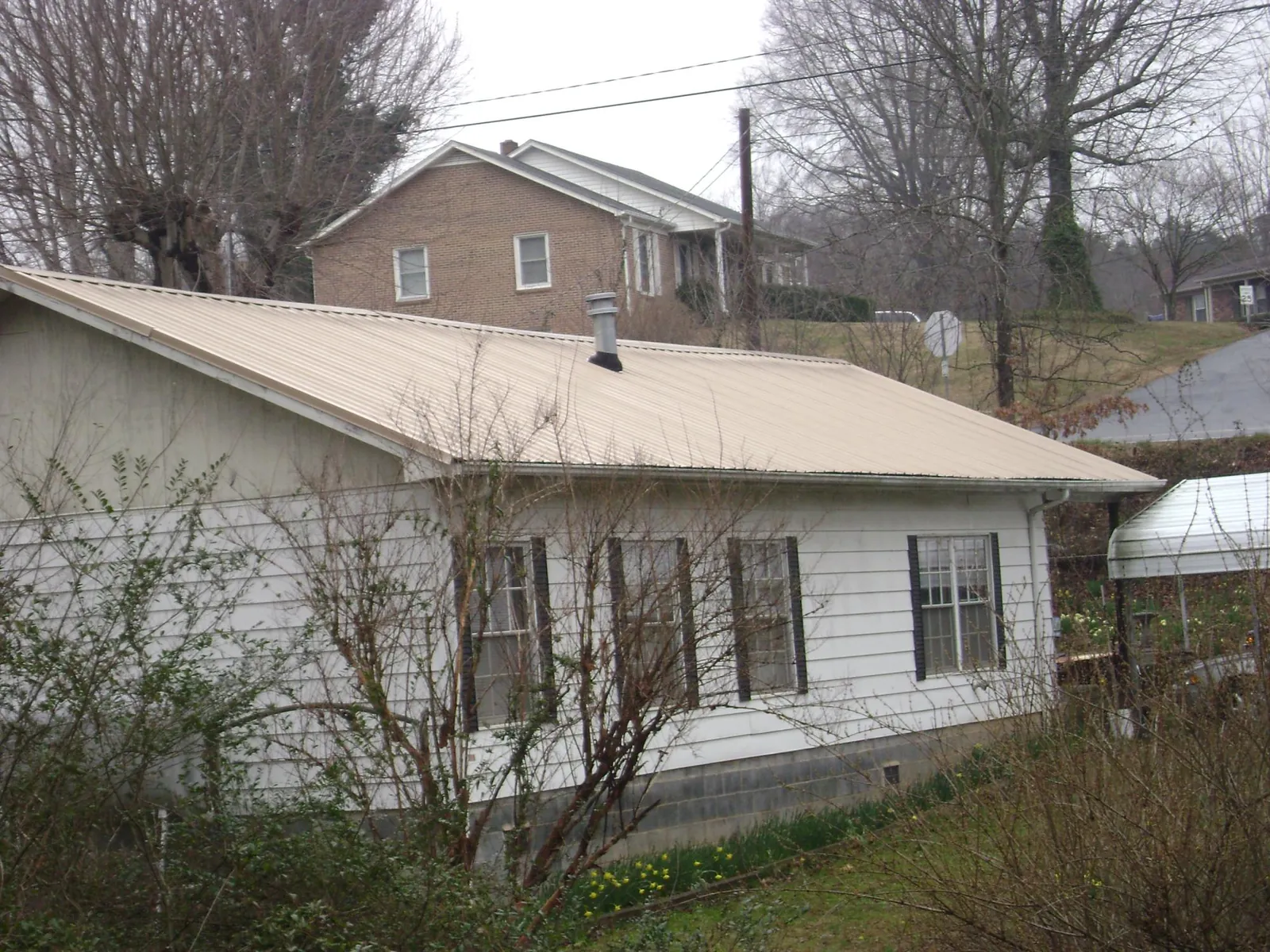 Tan metal roof on a white sided house set into a hillside — Commercial Roofing by Roofing Brothers in Sedro Woolley